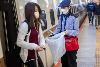 Japonya 'da bir tren istasyonunda çöp toplayan bir kadın, tren vagonunun yanında.