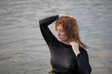 Suyun içinde siyah taytlı güzel kızıl saçlı genç bir kadının portresi.