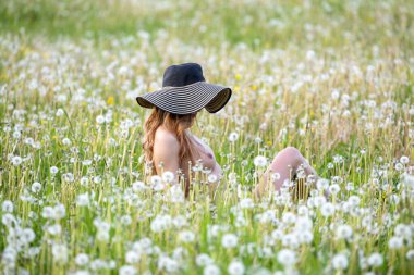Karahindiba otlağında şapkası olan güzel genç bir kadın.
