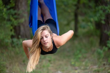 Genç bir kadın parkta havadan ipekle yerçekimi yogası yapıyor..