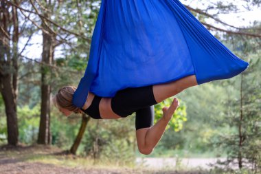 Genç bir kadın parkta havadan ipekle yerçekimi yogası yapıyor..
