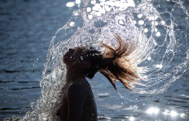 Gün batımında suda uzun saçlı genç bir kadın canlı ve sıcak bir sahne yaratır. Yüzme konsepti.