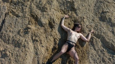 Çakıl çukurunda poz veren yuvarlak gözlükleri ve delikli bacakları olan güzel seksi kadın.