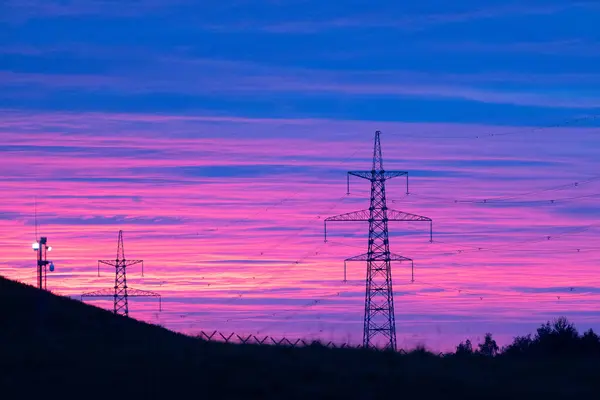 stock image Silhouetted High Voltage Towers Against a Stunningly Vibrant Pink and Purple Sunset Sky