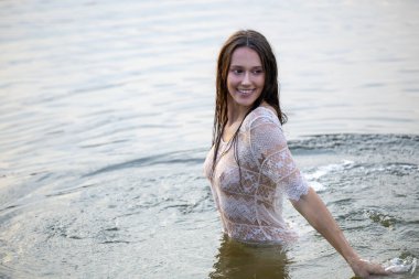 Beyaz şeffaf elbiseli çekici kız akşamları suda banyo yapıyor.