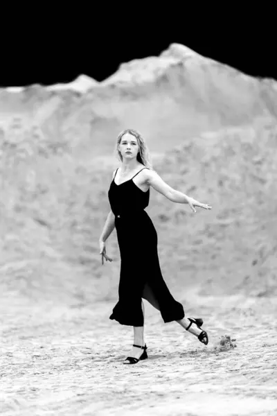 stock image Young beautiful woman in black dress and sand quarry background, in motion