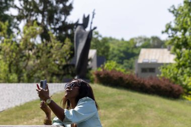 Güzel, koyu tenli bir kız huzurlu bir ortamda dolgun dudaklarına ruj sürüyor. Parktaki bankta bir güzellik anı.