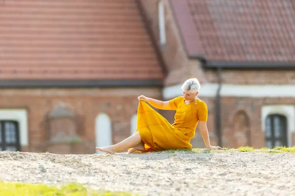 stock image A woman in a yellow dress sits on the ground outdoors in a good mood