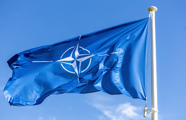 The blue NATO flag flutters against the blue sky. Military alliance symbol