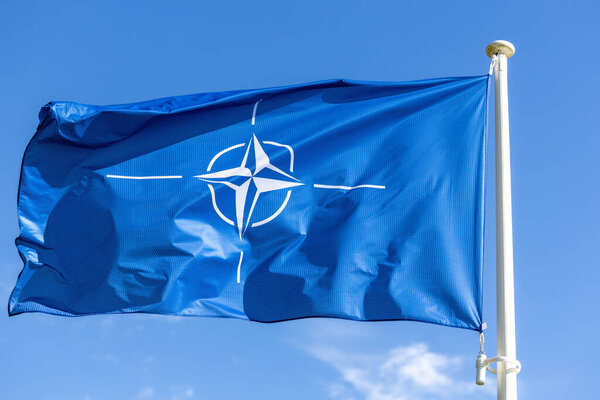 The blue NATO flag flutters against the blue sky. Military alliance symbol