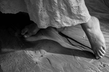 Çıplak ayaklar yumuşak kuma hafifçe dokunur, huzuru ve sadeliği çağrıştırır. Yumuşak ışık ve gölgeler sakin bir atmosfer yaratır.