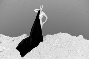 Doğada Zarafet: Karanlık Kumaşlı Bir Kadın Silueti Bir Arkaplan Su ve Kuma Karşı