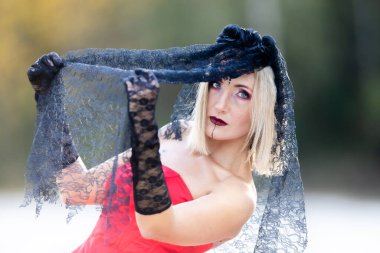 Blonde with Halloween makeup, black veil, red dress, and lace gloves: the elegance of darkness. Portrait of a beautiful woman clipart