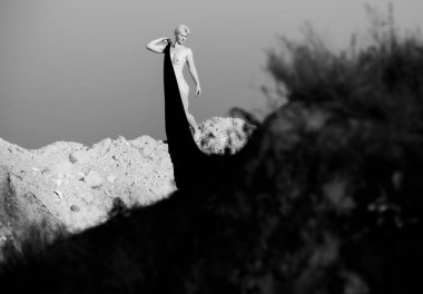 Doğada Zarafet: Karanlık Kumaşlı Bir Kadın Silueti Bir Arkaplan Su ve Kuma Karşı