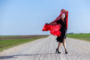 Elegant woman in a black dress and red scarf posing gracefully on a country road clipart