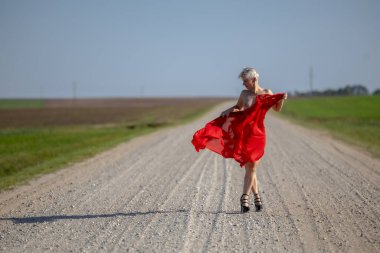 Cesaret ve Özgürlük: Kırsal bir yolda kırmızı bir eşarpla poz veren bir kadın, ufukta panoramik bir manzara