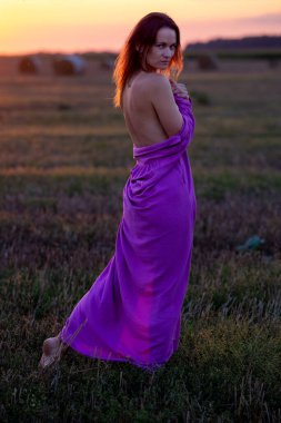 Young beautiful girl in a purple dress, bare back, in the light of the setting sun in the evening clipart