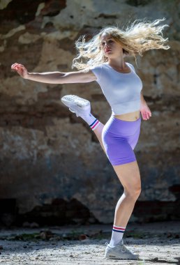 Beyaz bluzlu güzel bir sarışın enerjik bir atlayış yapıyor, dar şortlar giyiyor.