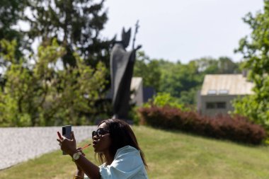 Güzel, koyu tenli bir kız huzurlu bir ortamda dolgun dudaklarına ruj sürüyor. Parktaki bankta bir güzellik anı.