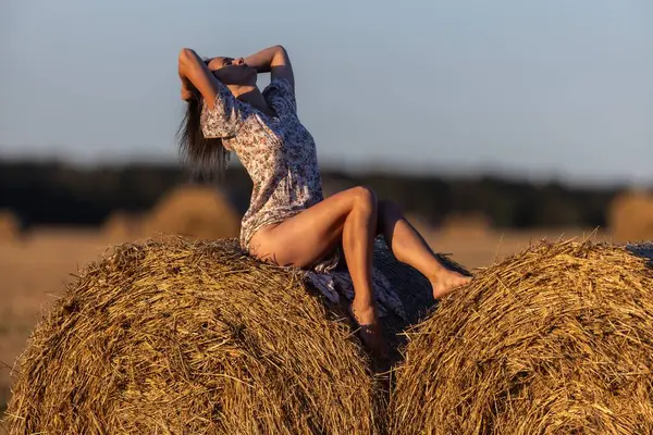Genç bir kadın saman balyalarında altın saatin tadını çıkarıyor, kırsal alanda gün batımında.