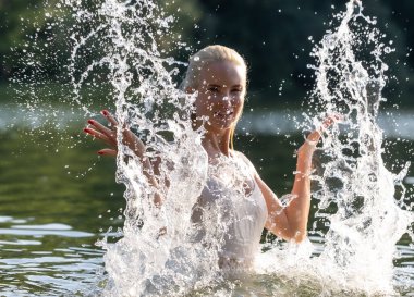 Beyaz bir yaz elbisesi içinde neşeli genç bir kadın güneşli bir günde doğal bir gölde su sıçratarak eğleniyor. Köpüklü su damlalarıyla havada yakalanan enerji hareketi doğada özgürlük, tazelik ve mutluluk hissi yaratıyor. Kişi başı