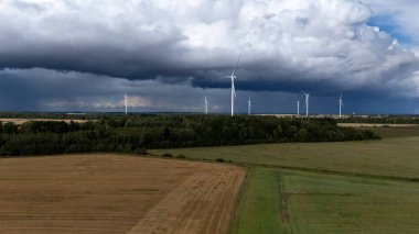 Modern bir rüzgar türbini karanlık ve bulutlu bir gökyüzüne karşı dimdik ayakta duruyor. Değişen hava koşullarında sürdürülebilirliği ve yeşil geleceği sembolize eden yenilenebilir enerji