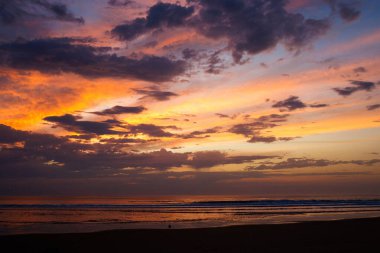 Gün batımı gökyüzü kıyı şeridi boyunca ıslak kumu yansıtıyor. Dramatik bulutlar ve parlayan renkler, doğa, seyahat ve rahatlama için ideal, barışçıl ama güçlü bir deniz manzarası yaratır.
