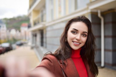 Sokakta ceketli genç bir iş kadını telefonunu elinde tutuyor ve selfie çekiyor..