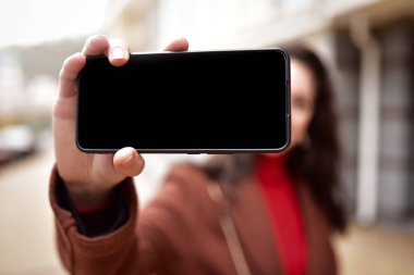 Sokakta yürürken selfie çeken genç bir kadın elinde siyah ekranlı bir akıllı telefon tutuyor. Boşluğu kopyala. Boş ekran