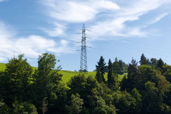 Yüksek voltaj hattı, yeşil çayırlı ve yeşil ağaçlı bir dağ. Elektrik giderek daha önemli hale geliyor, insanların enerji talebi artıyor, hava bulutlu.