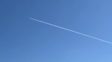 Mavi gökyüzünde uzun bir uçak yolu. Uçak mavi gökyüzünde uçuyor ve bir yoğunlaşma izi bırakıyor. Stok videosu. 4K