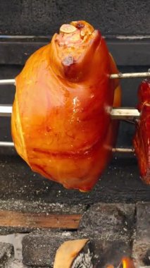 Açık ateşin üzerinde dönen altın füme jambonun videosu, ağız sulandıran bir barbekü sahnesinde cızırdayan sıvılar yakalamak, mükemmel ışıklandırma ve yoğun lezzet mutfak, yemek pişirme ve kırsal yemek temalı prodüksiyonlar için ideal.
