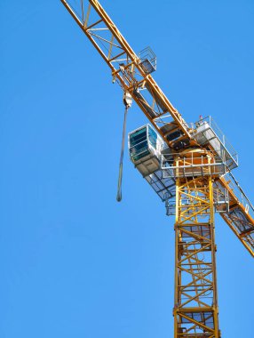 Açık mavi gökyüzüne karşı parlak sarı kule vinç. İnşaat alanlarında malzeme taşımak için kullanılan endüstriyel makineler. Modern mühendislik, kentsel gelişim ve inşaat endüstrisi.
