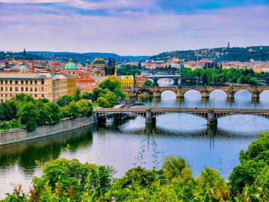 Prag 'daki Vltava Nehri' nin güzel manzarası, iki kıyıyı birbirine bağlayan zarif köprüler serisi. Çevredeki yeşillik nehri çevreleyen tarihi mimariyi tamamlıyor.