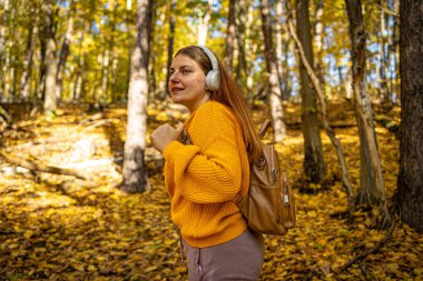 Parkta gülümseyen güzel beyaz bir kadının görüntüsü. Açık havada kulaklıkla müzik dinliyor. Cep telefonu kullanıyor..