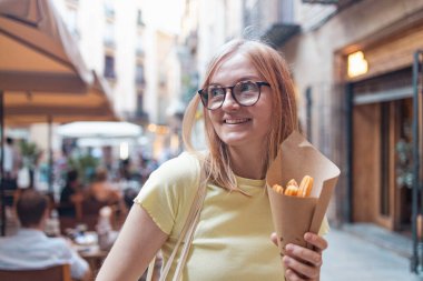 Neşeli sarışın kız geleneksel İspanyol lezzetli churros yiyor, Barcelona, İspanya 'daki sokak kafesinde çikolatalı bir kızarmış pasta.