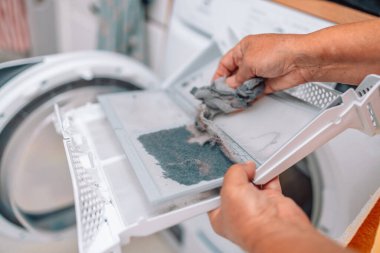 Çamaşır kurutma makinesi tarafından kapana kısılmış toz ve kir, kadın eli boya makinesinin kirli hava filtresini çıkarıyor. 