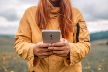 Genç bir kadın dağın tepesinde dinleniyor. Gezgin kız elinde bir cep telefonu tutuyor ve manzaranın fotoğraflarını çekiyor. Yan görünüm.