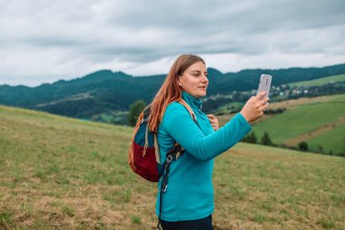 Akıllı telefon kullanan ve dağların tepesinde yürüyüp rahatlatan bir turist. Cep telefonuyla yaz yürüyüşü yapan genç bir gezgin kız doğada boş vakitlerin tadını çıkarıyor.. 