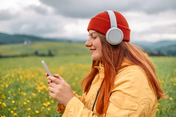 白种人美女头戴红帽子 穿着休闲装 快乐地笑着 独自远行 在山顶上远足 听音乐 欣赏大自然 — 图库照片