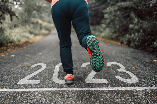 Numbers 2023 written on the road towards new goals in 2023 and female runners are starting to run. New Year 2023 with new ambitions, challenge, plans, goals and visions. High quality photo
