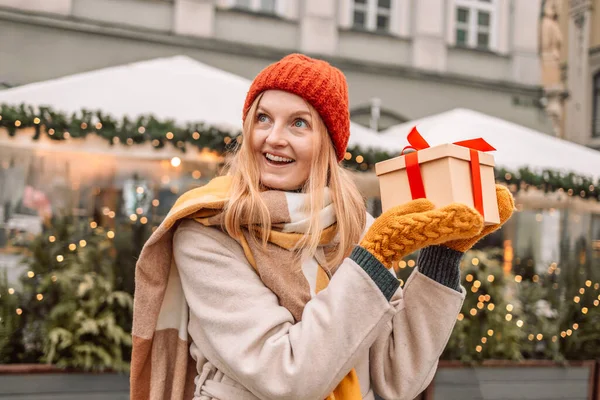Happy young attractive woman with paper bags and gift boxes in hands after Christmas shopping in mall. Cheerful beautiful girl hold shopping bags and present boxes in hands. Winter holidays sale
