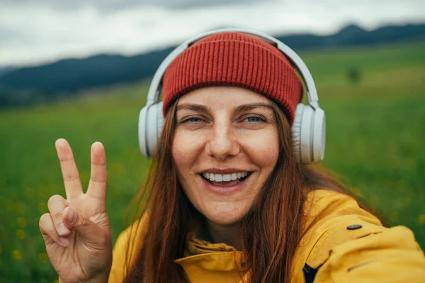 stock image Young happy woman traveler taking photo with smart phone in a good mood shows peace sign over the mountain