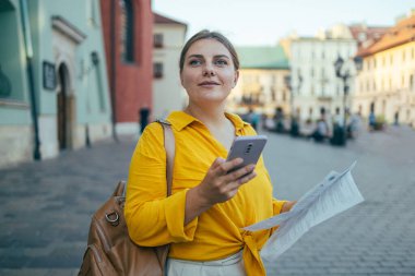 Şık giyinmiş gülümseyen bir kadın Central City caddesinde yürüyor ve telefonunu kullanıyor..