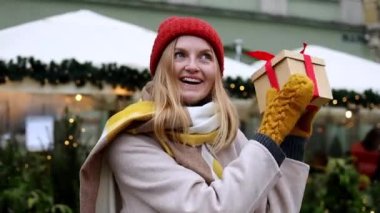 Son moda kıyafetler giyen sarışın bir kadının elinde hediye kutusuyla Krakow 'daki Noel Pazarı' na bakarken çekilmiş bir fotoğrafı. Hatıra satışı konsepti
