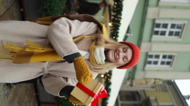 Son moda kıyafetler giyen sarışın bir kadının elinde hediye kutusuyla Krakow 'daki Noel Pazarı' na bakarken çekilmiş bir fotoğrafı. Hatıra satışı konsepti