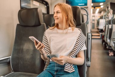Metroda cep telefonuna mesaj yazan gülümseyen sarışın bir kadının portresi.
