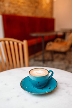 Kafe masasında kahve fincanındaki Latte sanatı. Köpükle çizilmiş Rosetta çiçeğinin yakın çekimi.