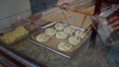 A female hand is greasing cinnamon rolls with a yolk. Homemade pastry on baking sheet lined with parchment. Cooking process of traditional swedish buns kanelbullar. Close up. 