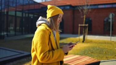 Caucasian young female student freelancer relaxing in city park after classes at university college, d talking on the smartphone, surfing social media.